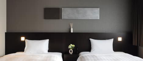 Quarto de hotel com duas camas, cabeceira escura e luminária fixada na parede.