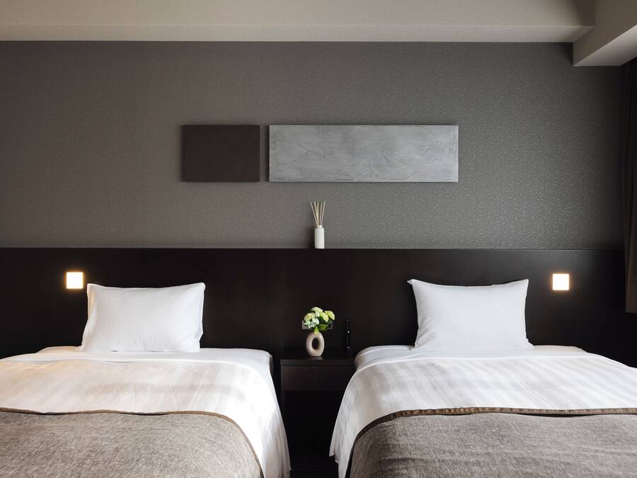A hotel room with two beds, a dark headboard, and a wall-mounted light fixture.