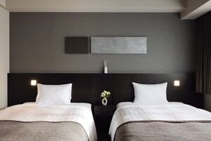 Habitación de hotel con dos camas, cabecero oscuro y lámpara fijada a la pared.