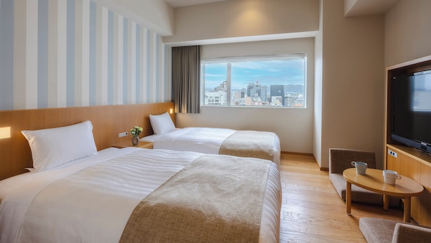 A hotel room with two beds, a TV, a small table, and a window with a city view. - Hiroshima Washington Hotel (Hiroshima)