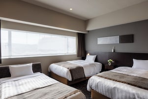Ein Hotelzimmer mit drei Betten, einem großen Fenster, einem Kopfteil mit Leuchte und einem Wandbild.