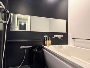 A modern bathroom with a bathtub, a mirror, a towel rack, and a trash bin. - Hiroshima Washington Hotel (Hiroshima)
