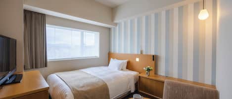 Une chambre d’hôtel avec un lit, un bureau, une chaise, une petite table et une fenêtre avec des rideaux.