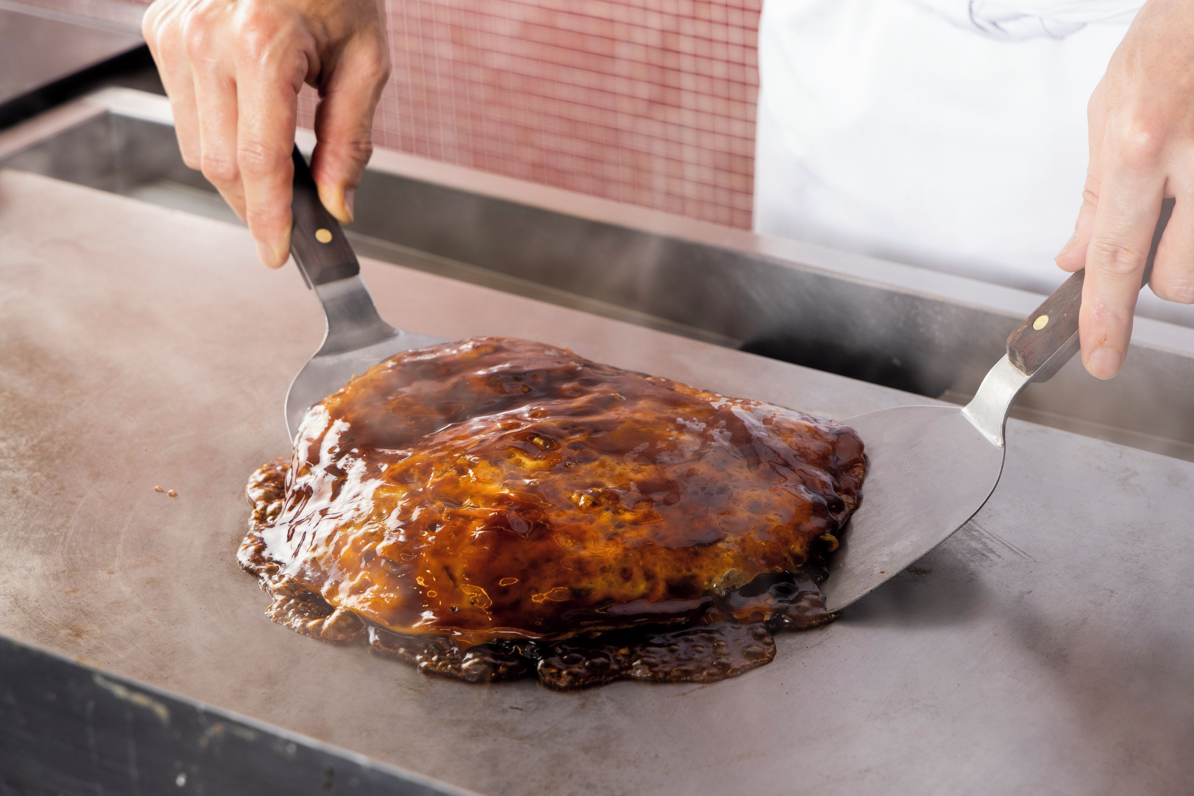 A person using a spatula to serve a glazed meat dish on a flat surface.