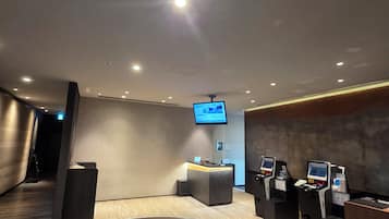 A modern lobby with a reception desk, a mounted TV screen, and self-service kiosks.