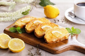 A wooden board with lemon slices and mint leaves, a whole lemon, and a cup of coffee on a table.