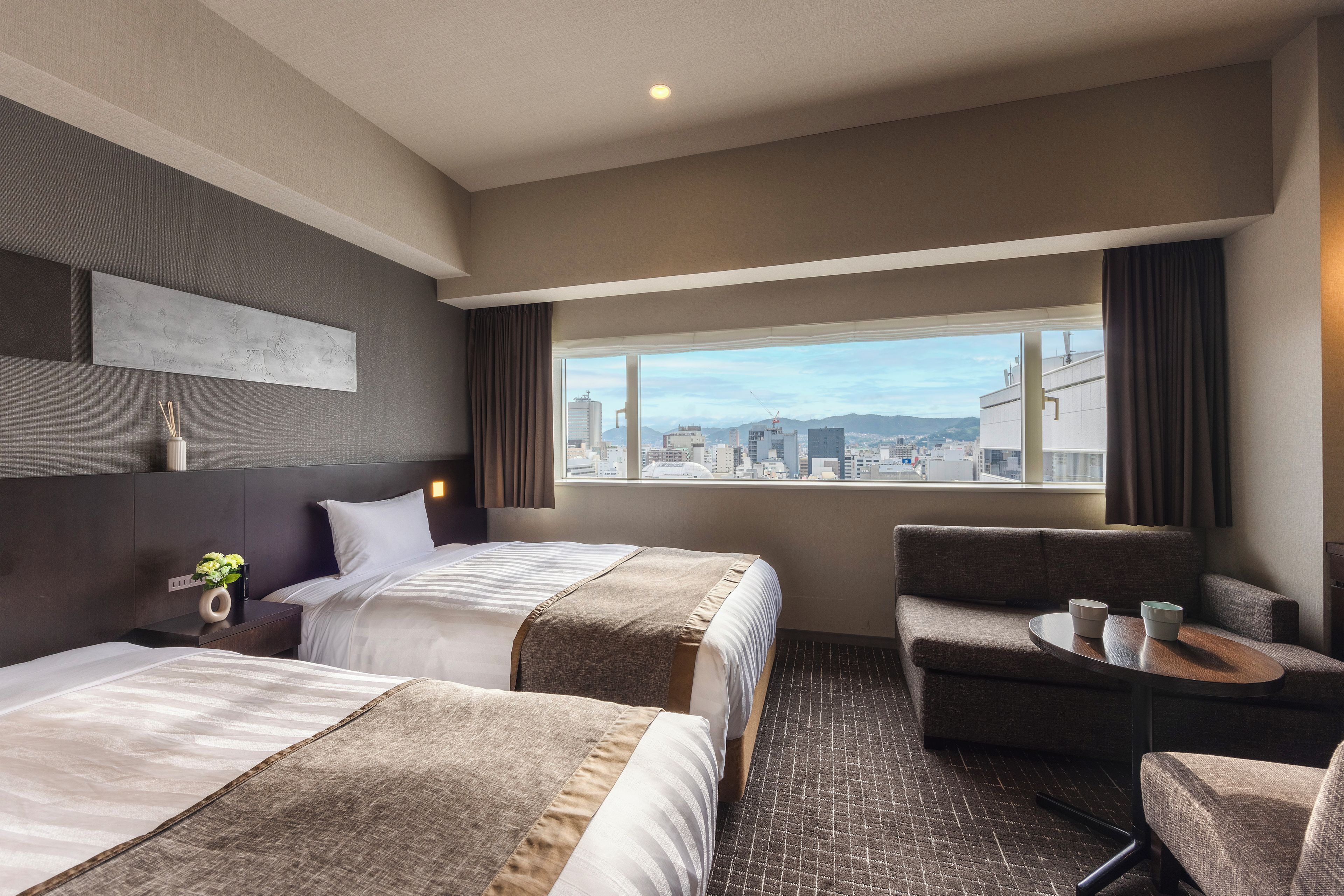 Habitación de hotel con dos camas, un sofá, una mesita y vistas a la ciudad.