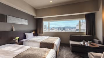 Habitación de hotel con dos camas, un sofá, una mesita y vistas a la ciudad.