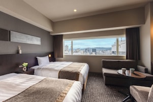 Habitación de hotel con dos camas, un sofá, una mesita y vistas a la ciudad.