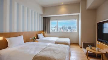 Habitación de hotel con dos camas, televisión, una mesita y ventana con vista a la ciudad.
