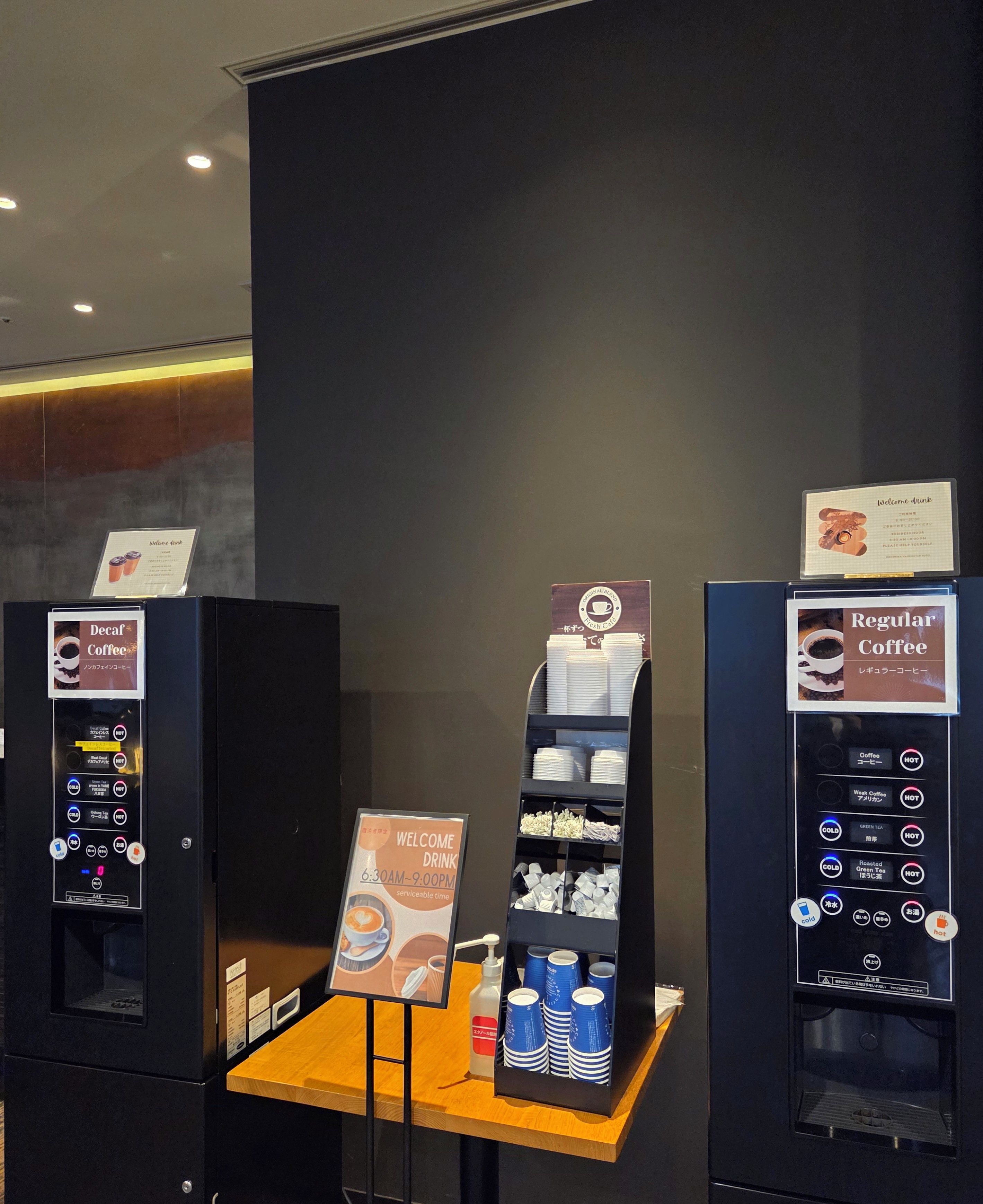 A coffee vending area with two machines, one for decaf and one for regular coffee, and a display of disposable cups.
