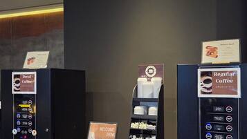 A coffee vending area with two machines, one for decaf and one for regular coffee, and a display of disposable cups.