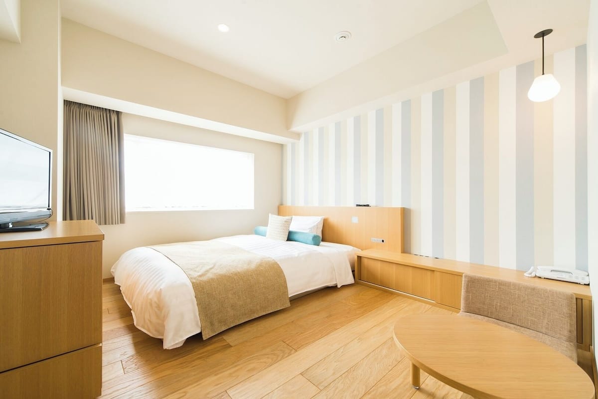 Quarto de hotel com cama, televisão, escrivaninha e janela.