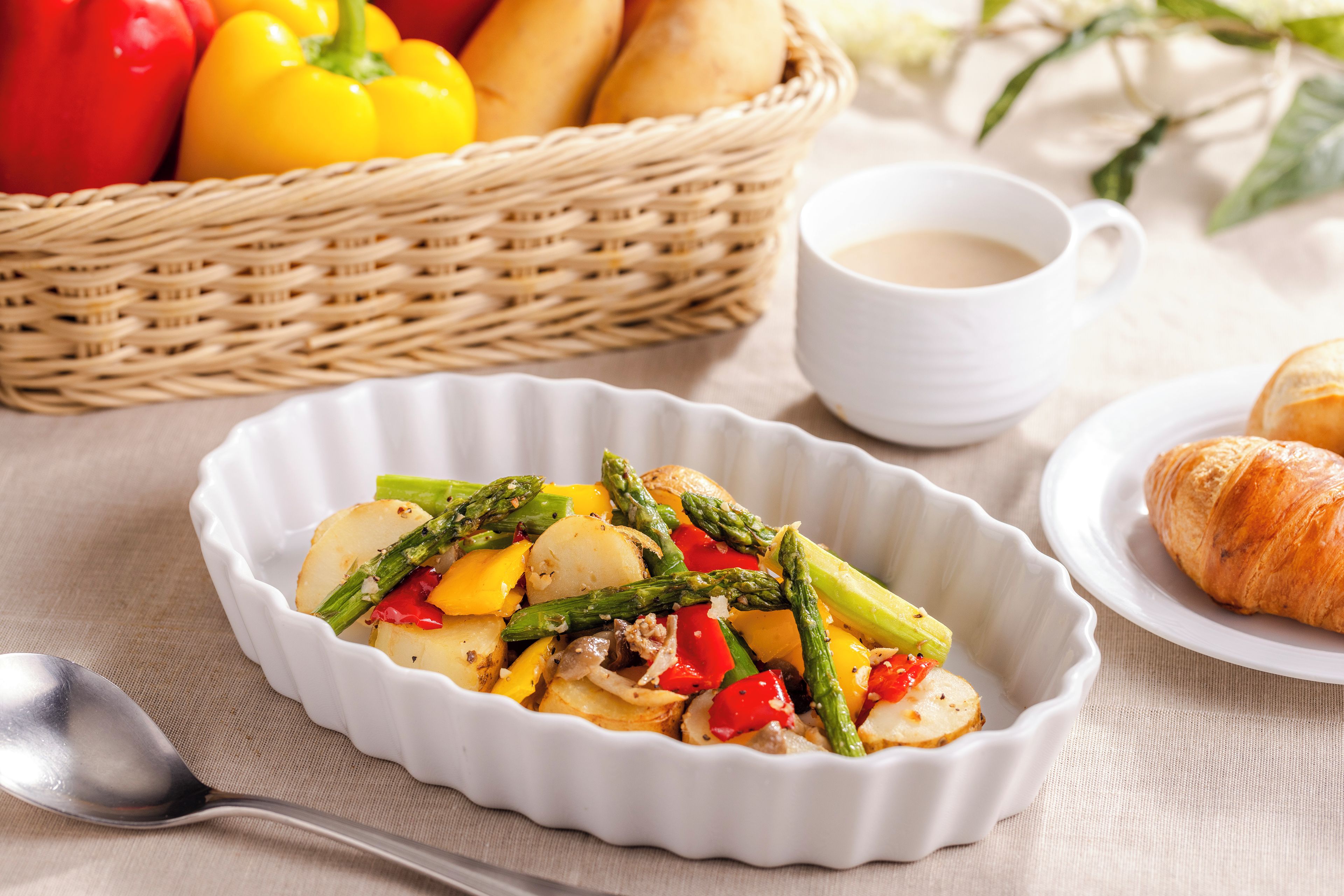 A white ceramic dish with a variety of vegetables and a croissant on a plate.