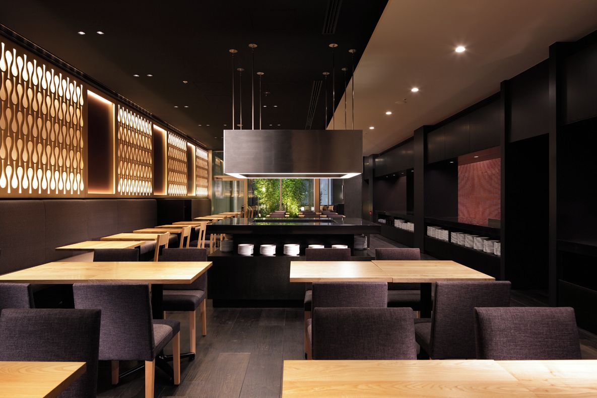 A modern restaurant interior with multiple dining tables and chairs, a central light fixture, and a view of greenery outside.