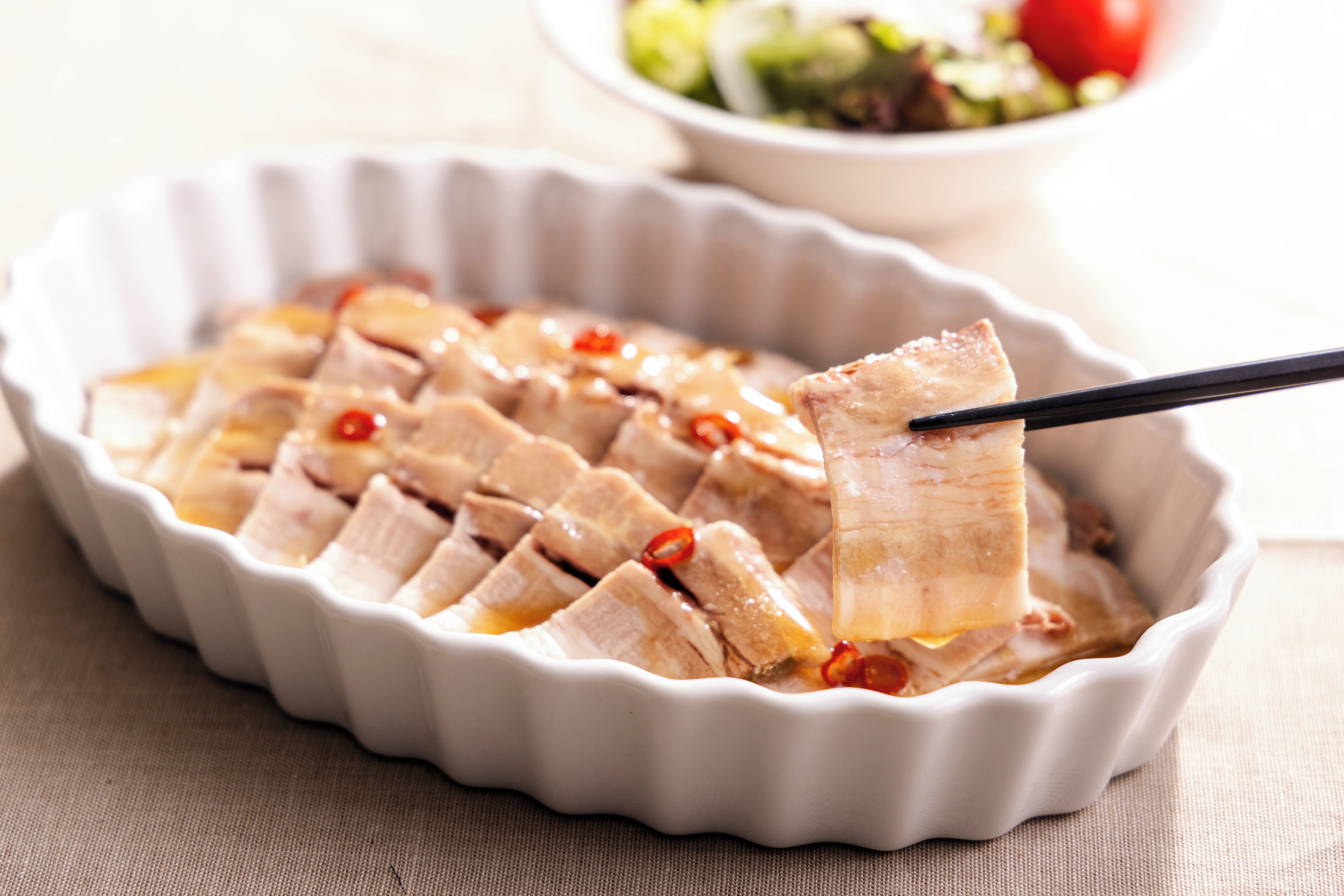 A white ceramic dish with sliced meat and chili peppers.