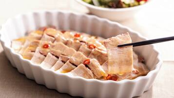 A white ceramic dish with sliced meat and chili peppers.