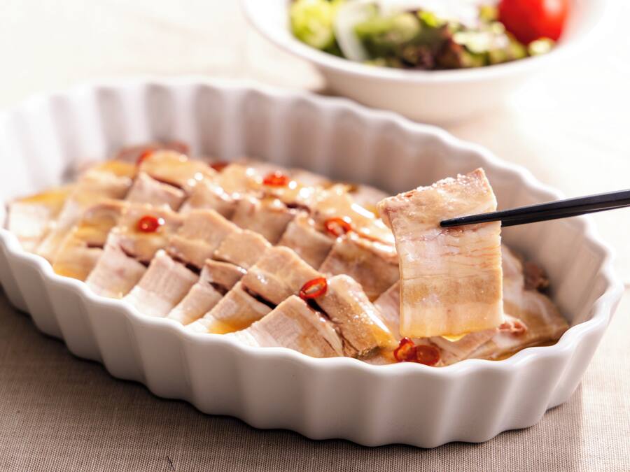A white ceramic dish with sliced meat and chili peppers.