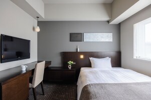 Habitación de hotel con cama, escritorio con silla, televisión de pantalla plana, mesita con un florero y dos obras de arte colgadas en la pared.