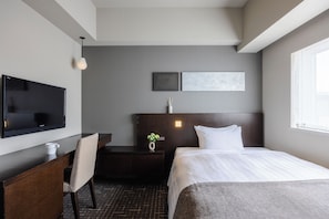 A hotel room with a bed, a desk with a chair, a flat-screen TV, a small table with a vase of flowers, and two wall-mounted artworks. - Hiroshima Washington Hotel (Hiroshima)