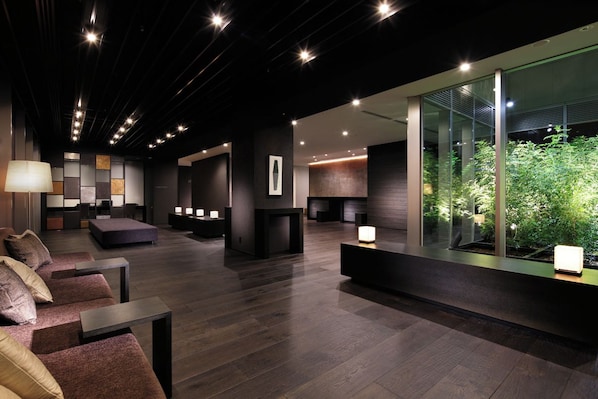 A modern lobby with a reception desk, seating area, and a glass wall with a view of greenery. - Hiroshima Washington Hotel (Hiroshima)