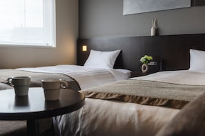 Habitación de hotel con dos camas, una mesita de noche con una taza, un florero con flores y una lámpara de pared.