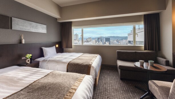 A hotel room with two beds, a sofa, a small table, and a view of the city. - Hiroshima Washington Hotel (Hiroshima)