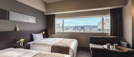A hotel room with two beds, a sofa, a small table, and a view of the city.