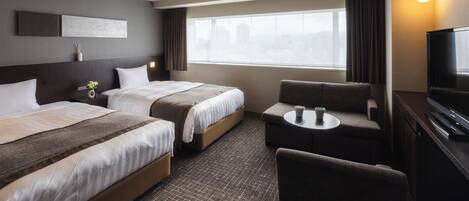 A hotel room with two beds, a sofa, a TV, and a window with curtains.