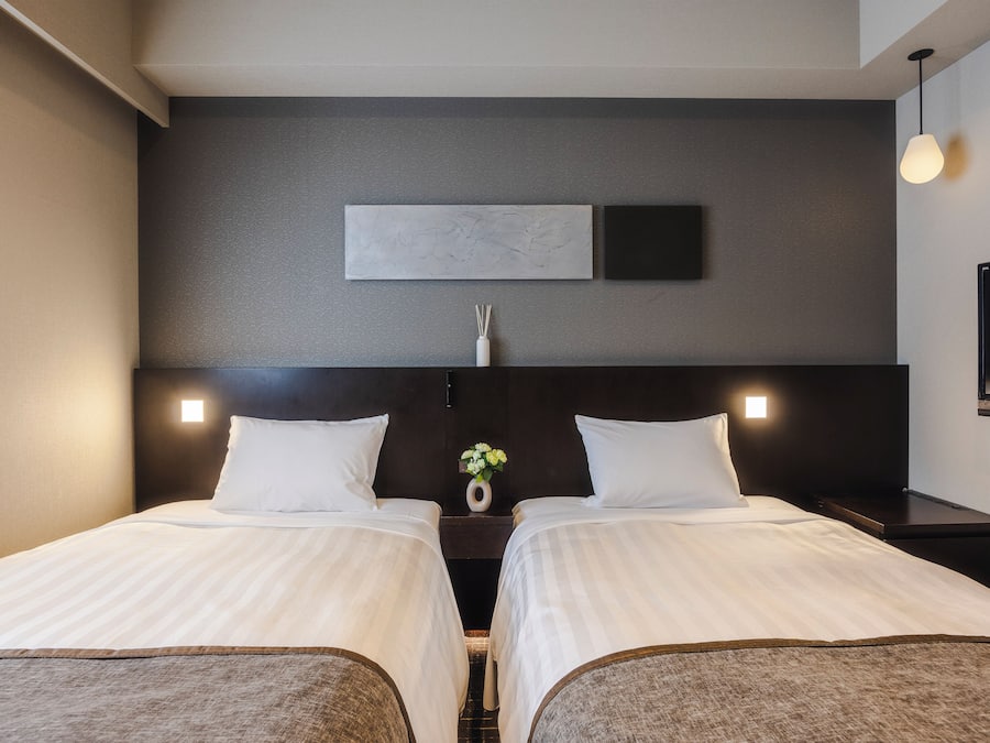 A hotel room with two beds, a nightstand with a vase of flowers, a flat-screen TV, and a painting on the wall.