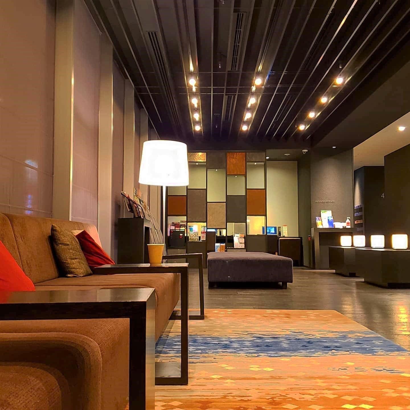 A hotel lobby with a sofa, ottoman, and a reception desk.
