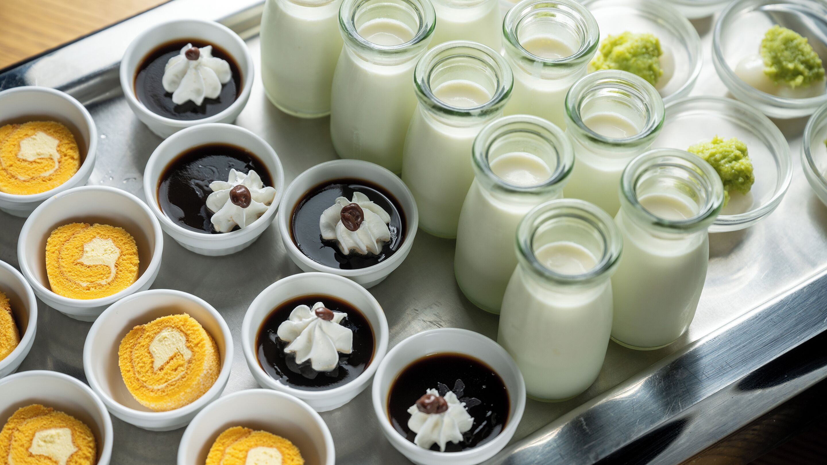 A tray with various food items including bowls of dessert and bottles of milk.