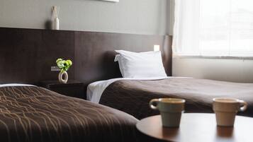 A hotel room with two beds, a nightstand with a vase of flowers, and a table with two cups.