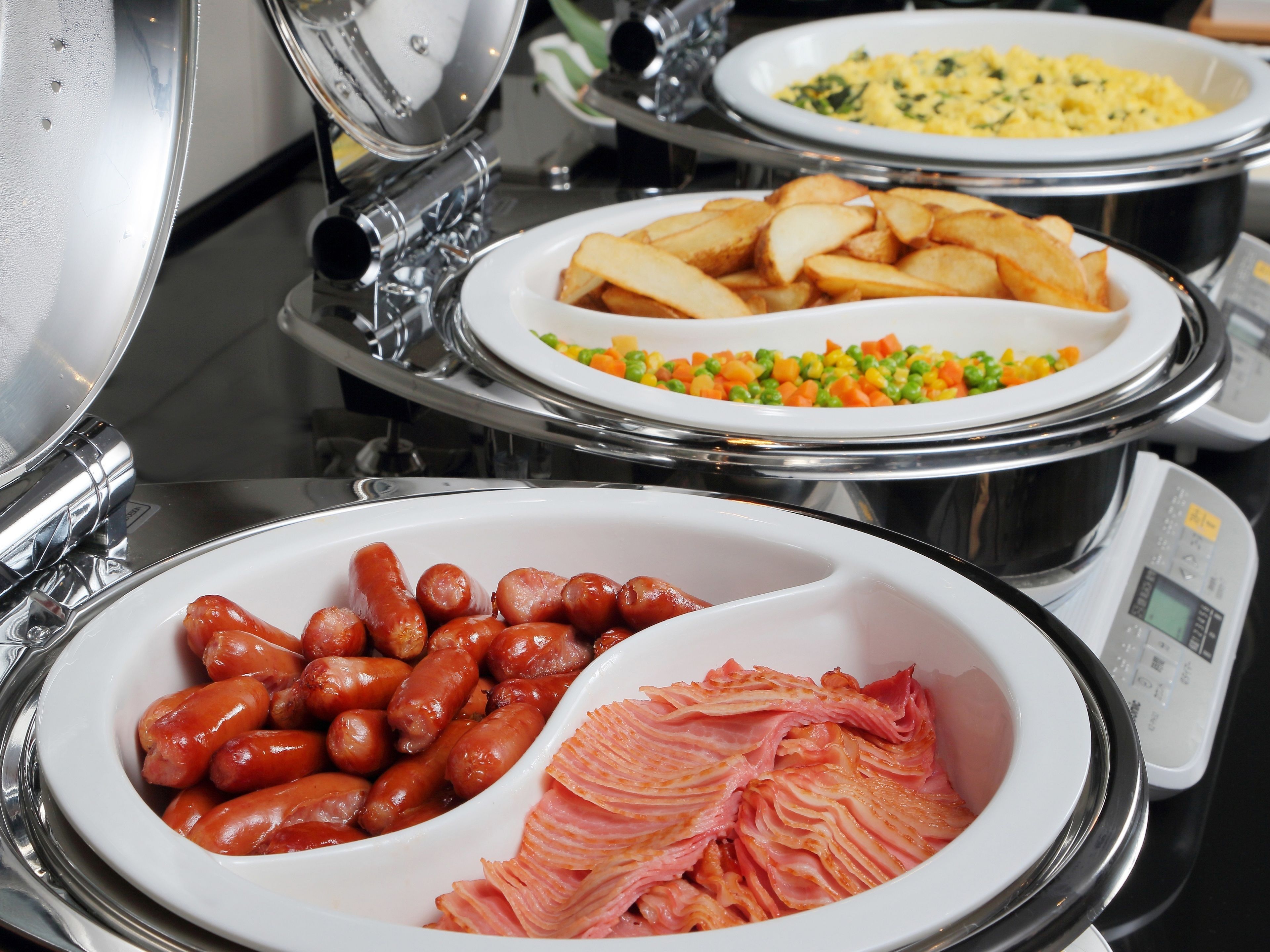 A buffet with various dishes including sausages, ham, potatoes, and mixed vegetables.