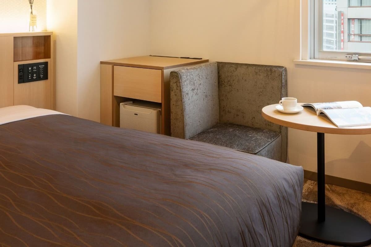 Habitación de hotel con cama, escritorio, silla y ventana.