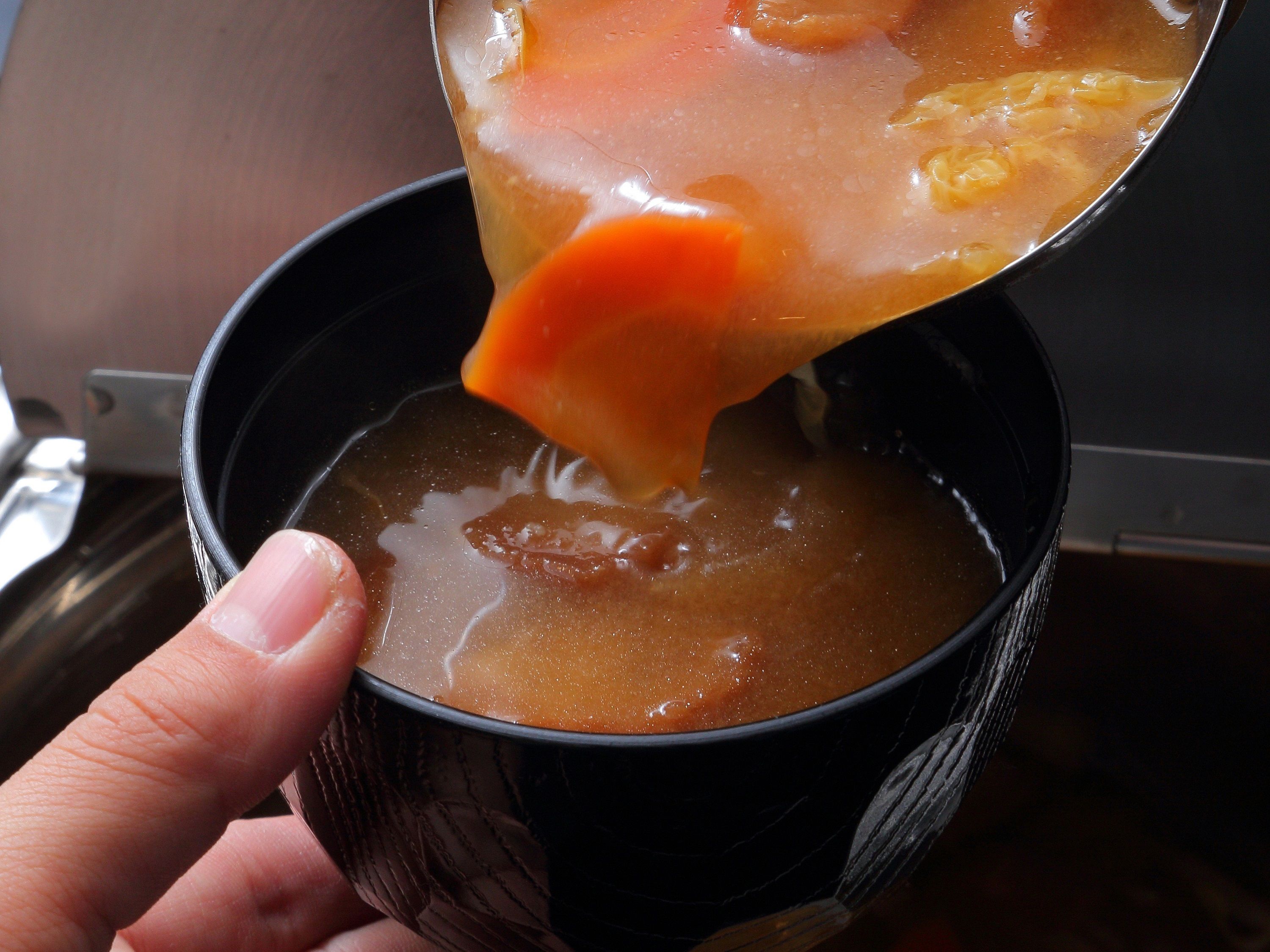 A hand holding a cup with a dark interior and a spoon lifting a thick, orange-colored liquid from it.