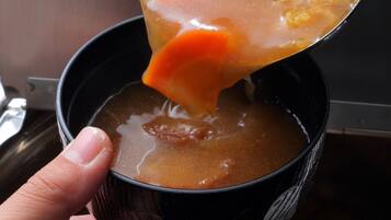 A hand holding a cup with a dark interior and a spoon lifting a thick, orange-colored liquid from it.
