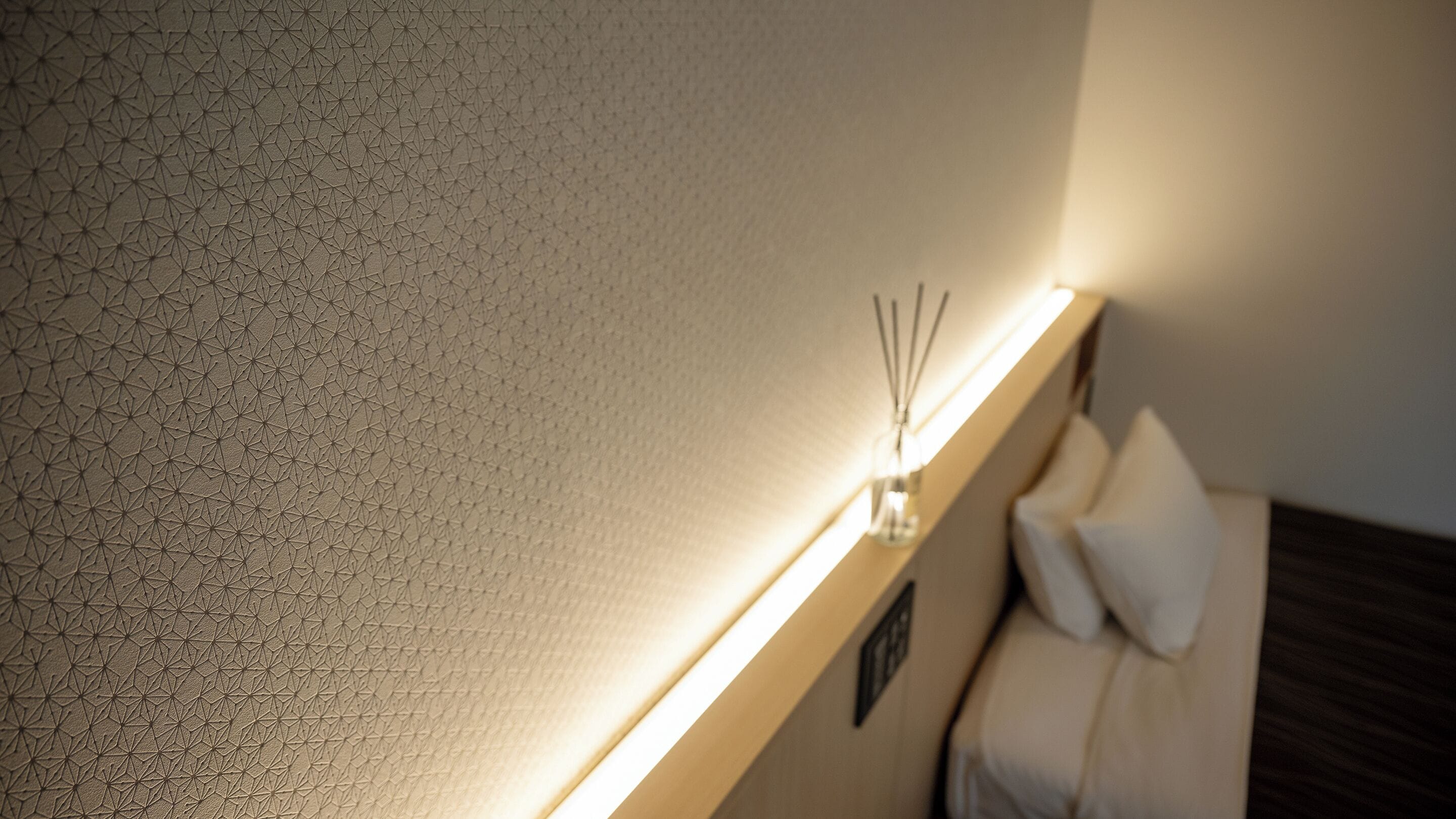 A room with a textured wall, a bedside table with a lamp, and a bed with pillows.
