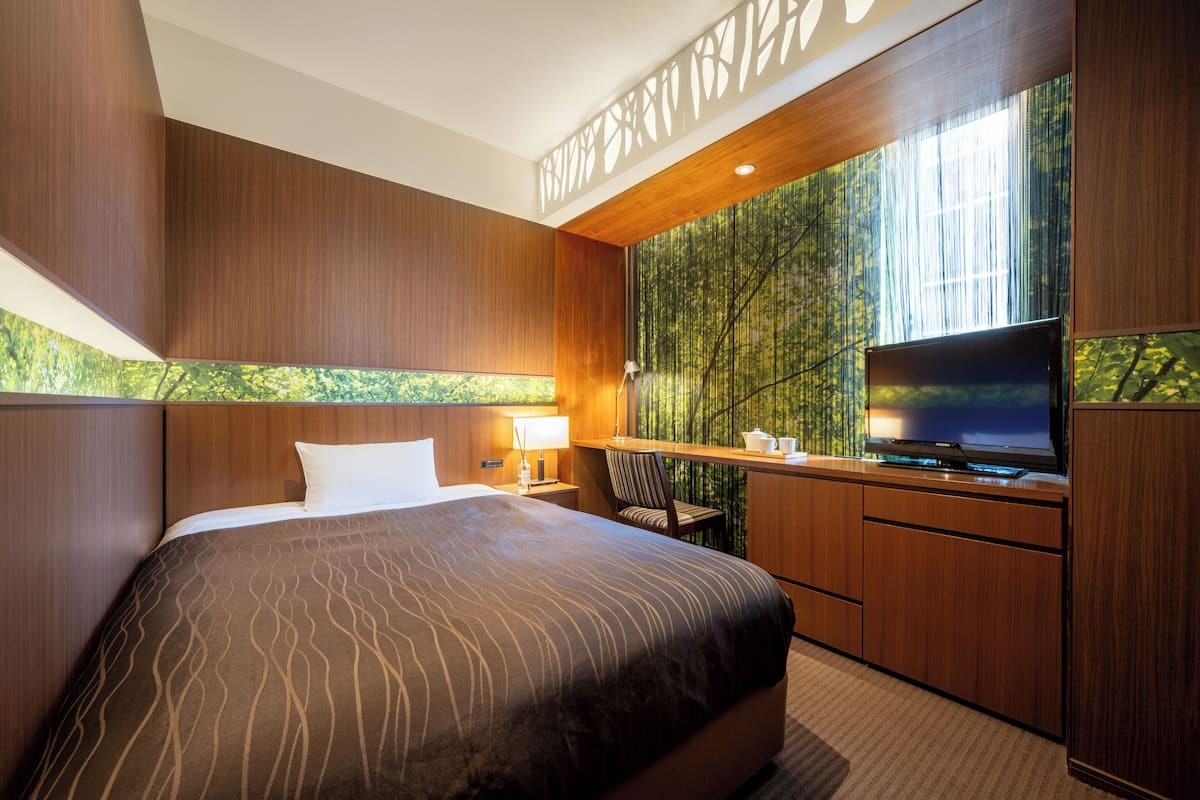 Habitación de hotel con una cama grande, televisor, escritorio y ventana con vista a árboles.