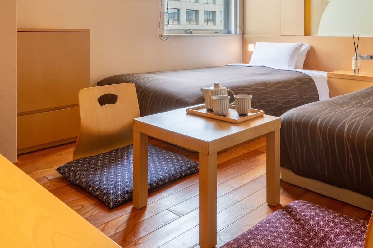 Una habitación de hotel con dos camas, una mesita con una bandeja de té y una silla.