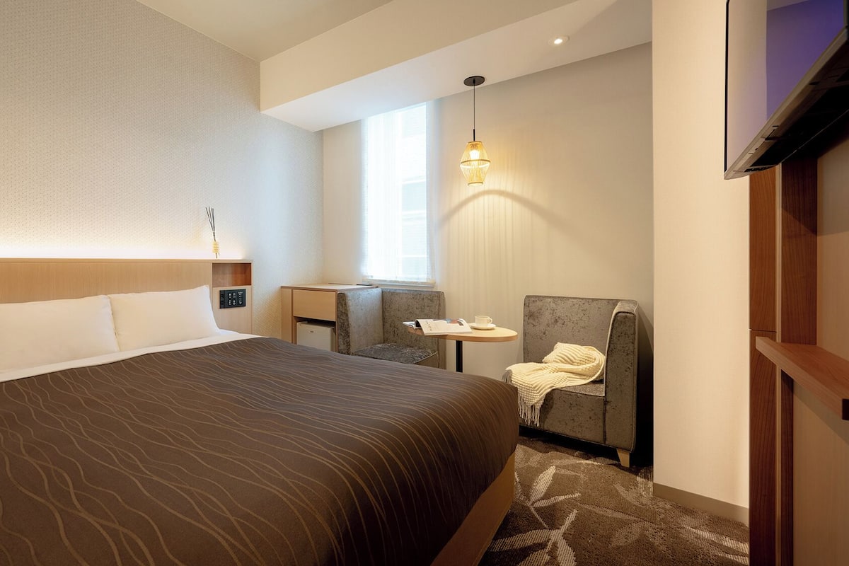 A hotel room with a large bed, a desk, a chair, a TV, and a window.