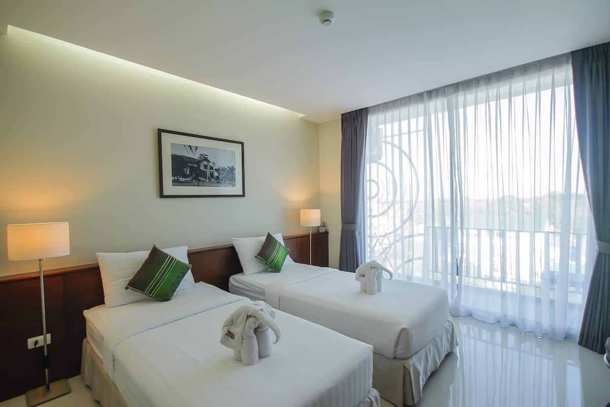 Habitación de hotel con dos camas, un cuadro en la pared y un ventanal con cortinas translúcidas.