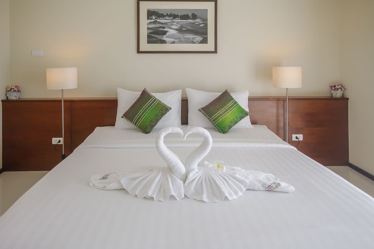 Una habitación de hotel con una cama bien hecha, dos almohadas, un cuadro en la pared y una lámpara a cada lado de la cama.