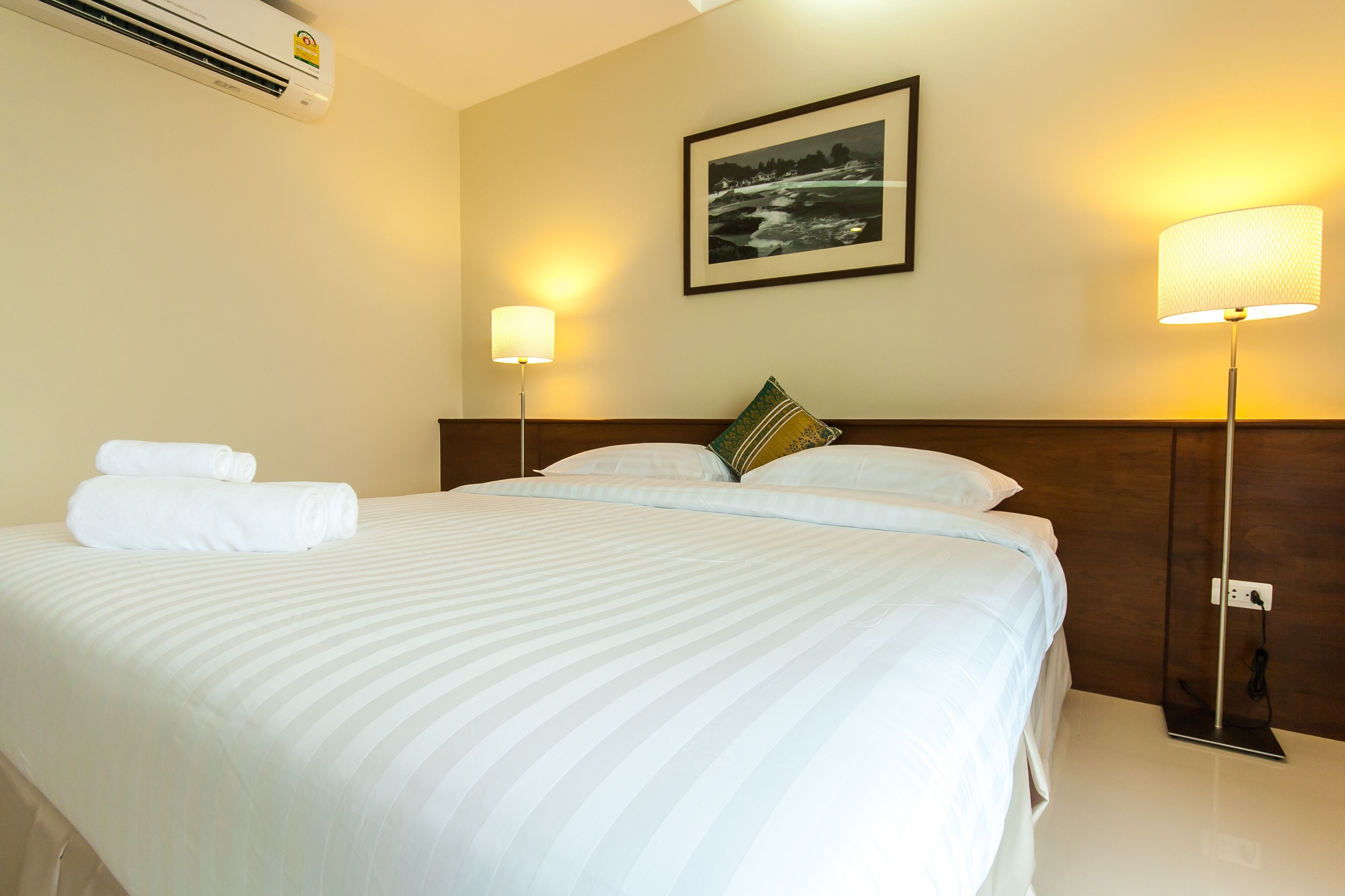 Habitación de hotel con una cama grande, dos lámparas de noche, un cuadro enmarcado en la pared y un aire acondicionado instalado en la pared.