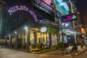 A hotel with a glass facade, outdoor seating, and a neon sign. - Baan Nilrath Hotel (Hua Hin)