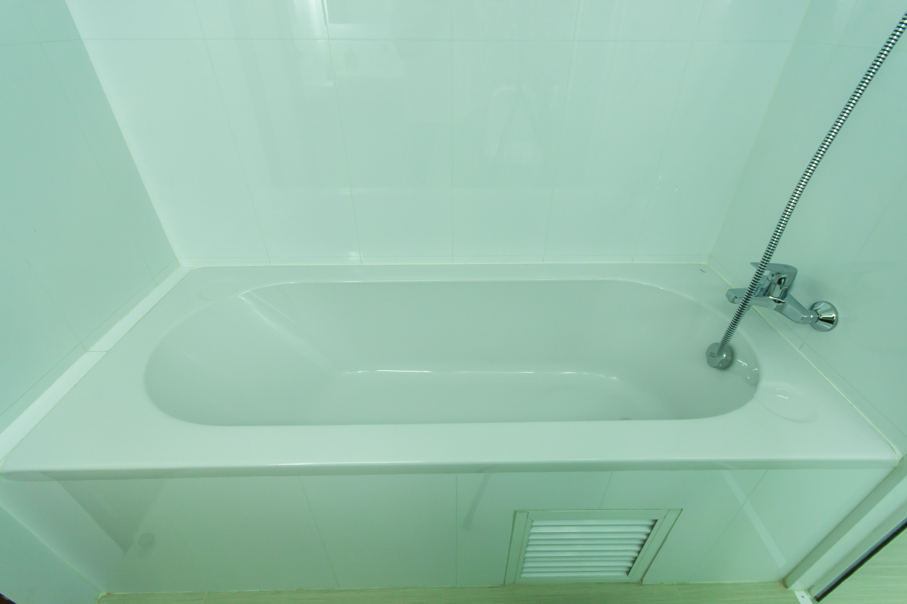 A bathroom with a white bathtub, a showerhead, and a vent.