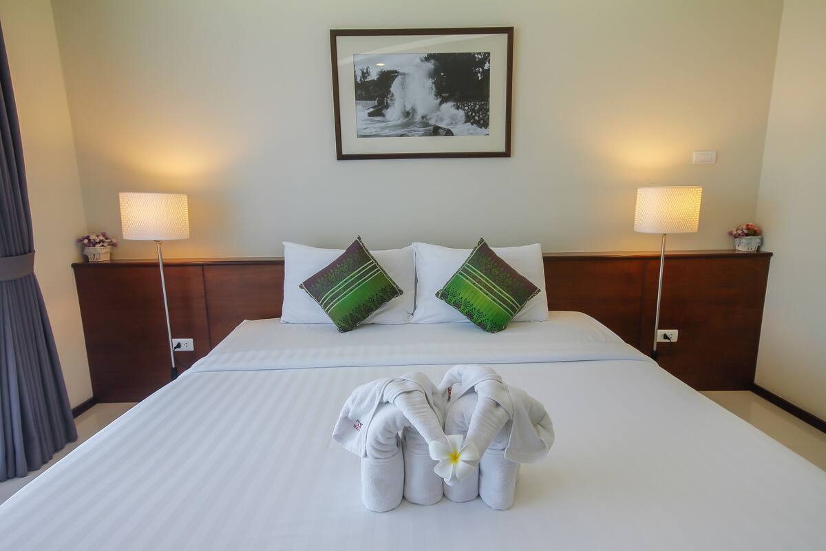 Una habitación de hotel con una cama bien hecha, dos almohadas, dos lámparas de noche y un cuadro enmarcado en la pared.