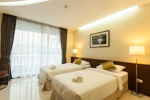 A hotel room with two beds, a chair, a lamp, and a window with curtains.