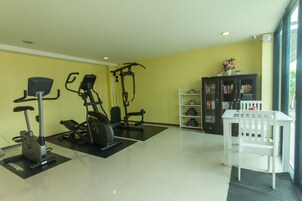 Un gimnasio en casa con equipo de ejercicio, una silla blanca y una estantería.