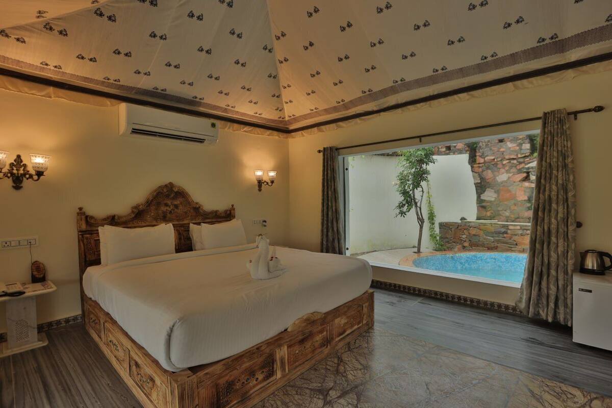 A spacious bedroom with a large bed, a view of an outdoor pool, and a stone wall.